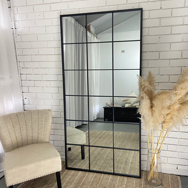 The Grid Mirror in black, industrial window-style metal frame leaning against a wall
