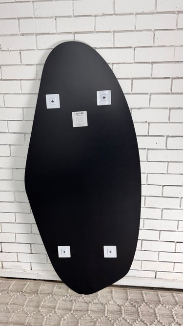 Frameless pebble shaped mirror leaning against a wall