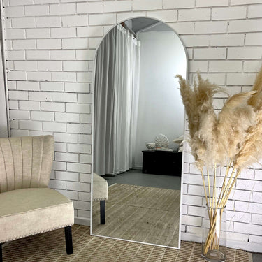 Minimalist white arch mirror leaning against a wall