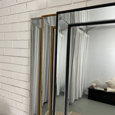 Tall beaded floor mirror leaning against a wall