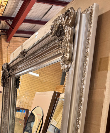 Extra large carved wooden floor mirror against a wall