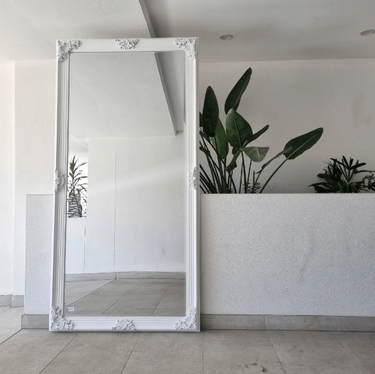 Extra large carved wooden floor mirror against a wall