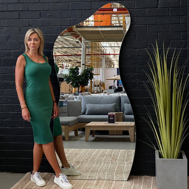 Frameless hourglass-shaped mirror leaning against a wall